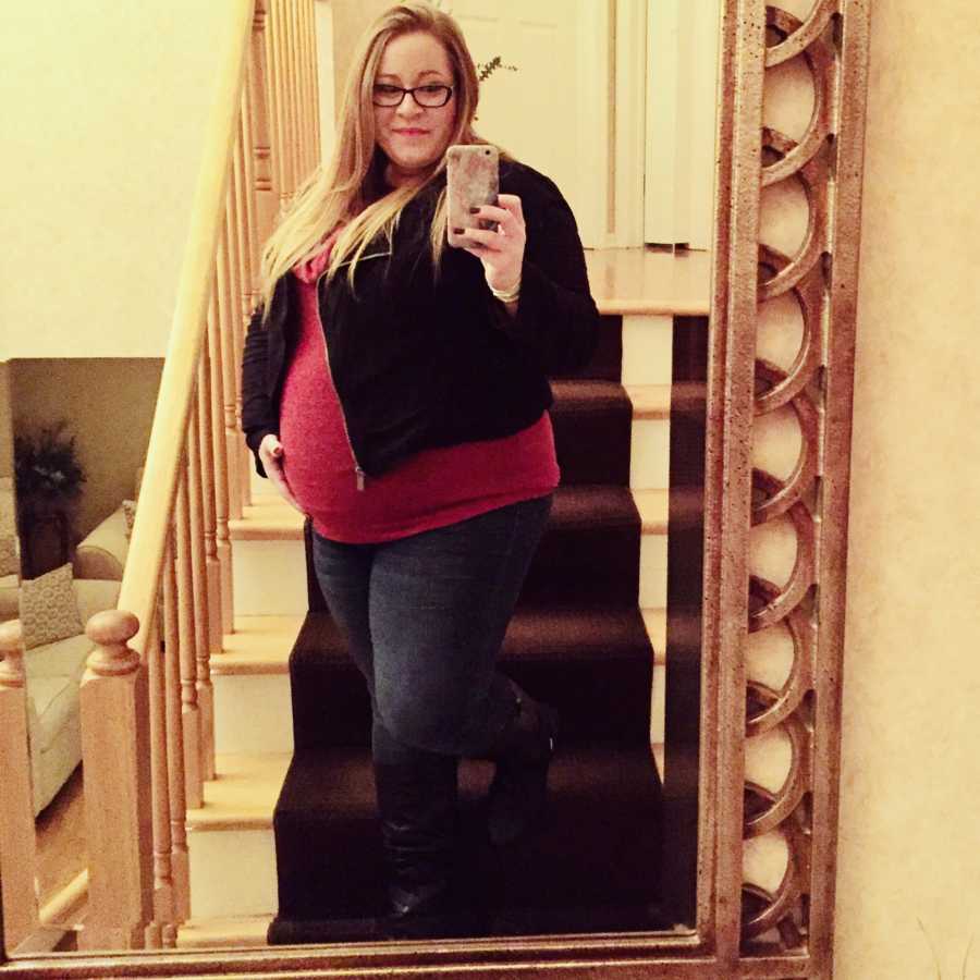 Pregnant woman stands on steps of home smiling in mirror selfie