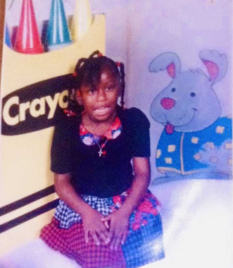 Little girl whose uncle raped her sits in dress with oversized box of crayons behind her