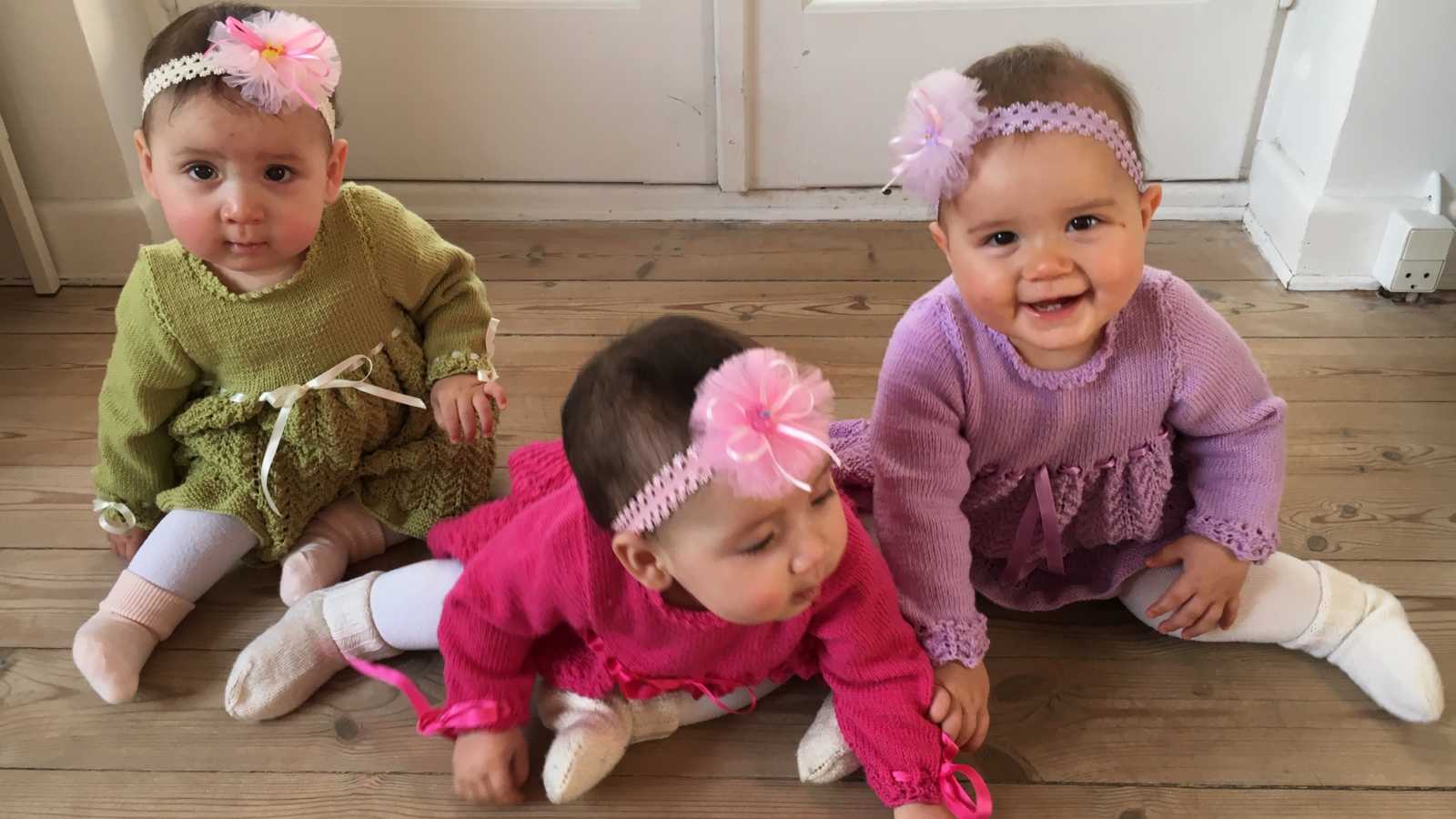 Baby triplets with two dads sits smiling on floor of home