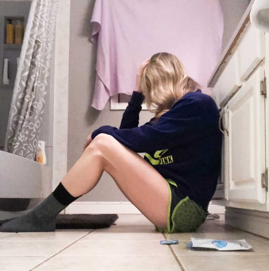 Woman who has trouble getting pregnant sits on floor of bathroom resting her head on her hand