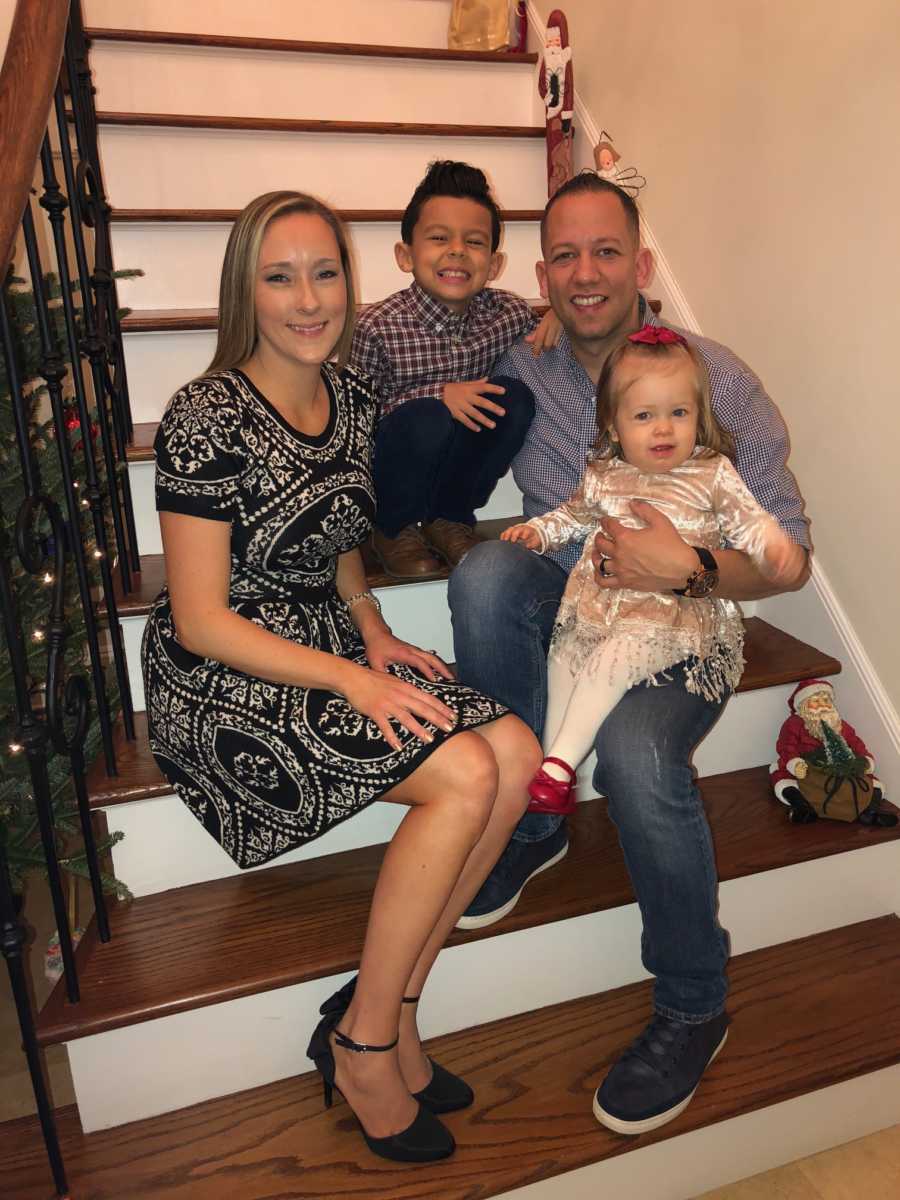 Man sits on step of home beside his son, wife, and their daughter