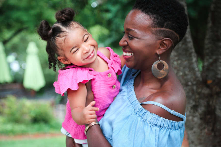 Mother stands smiling outside holding daughter with prosthetic eyes