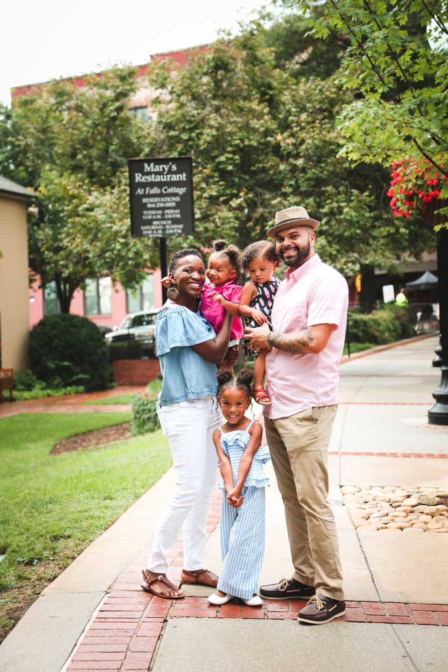 Husband and wife stand on side walk with their three daughters