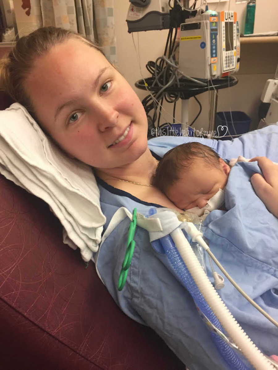 Mother lays in hospital smiling as intubated newborn lays on her chest