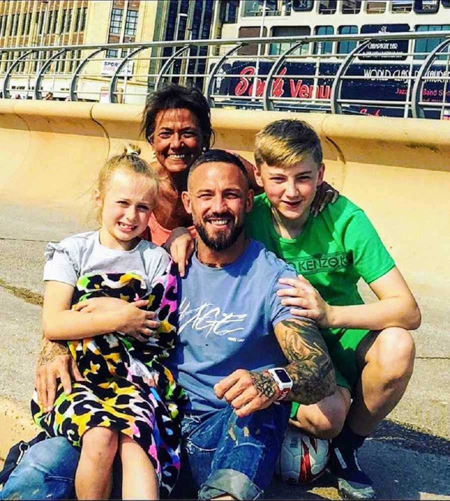 Man who is a recovered addict sits outside smiling with two kids and wife