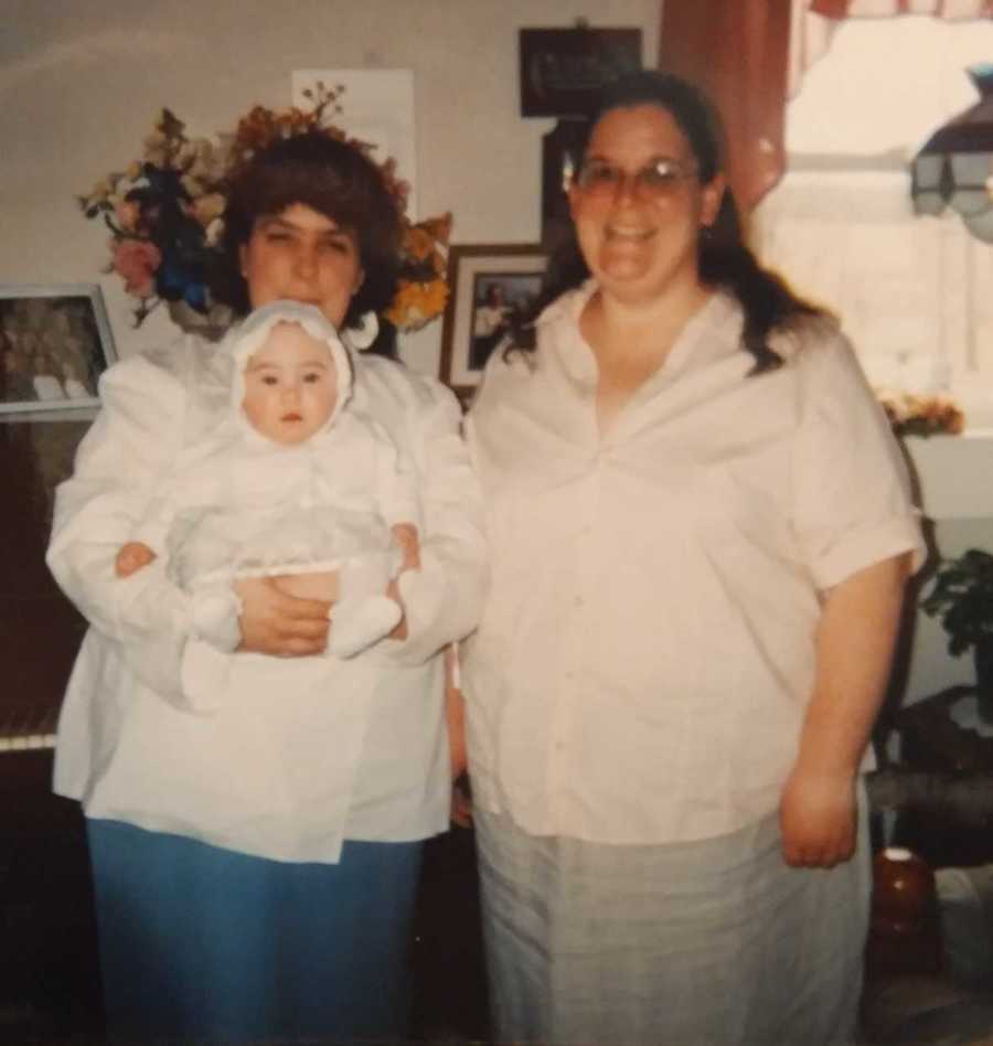 Woman stands in home beside her wife as she holds their baby 