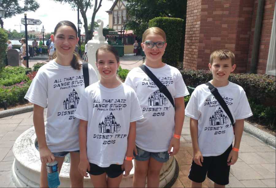 Four young kids stand smiling in matching t-shirts for Disney trip