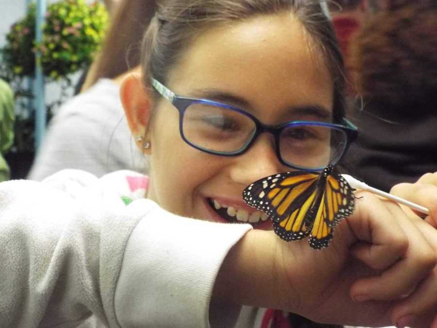 Young girl smiles at Monarch butterfly sitting on her hand