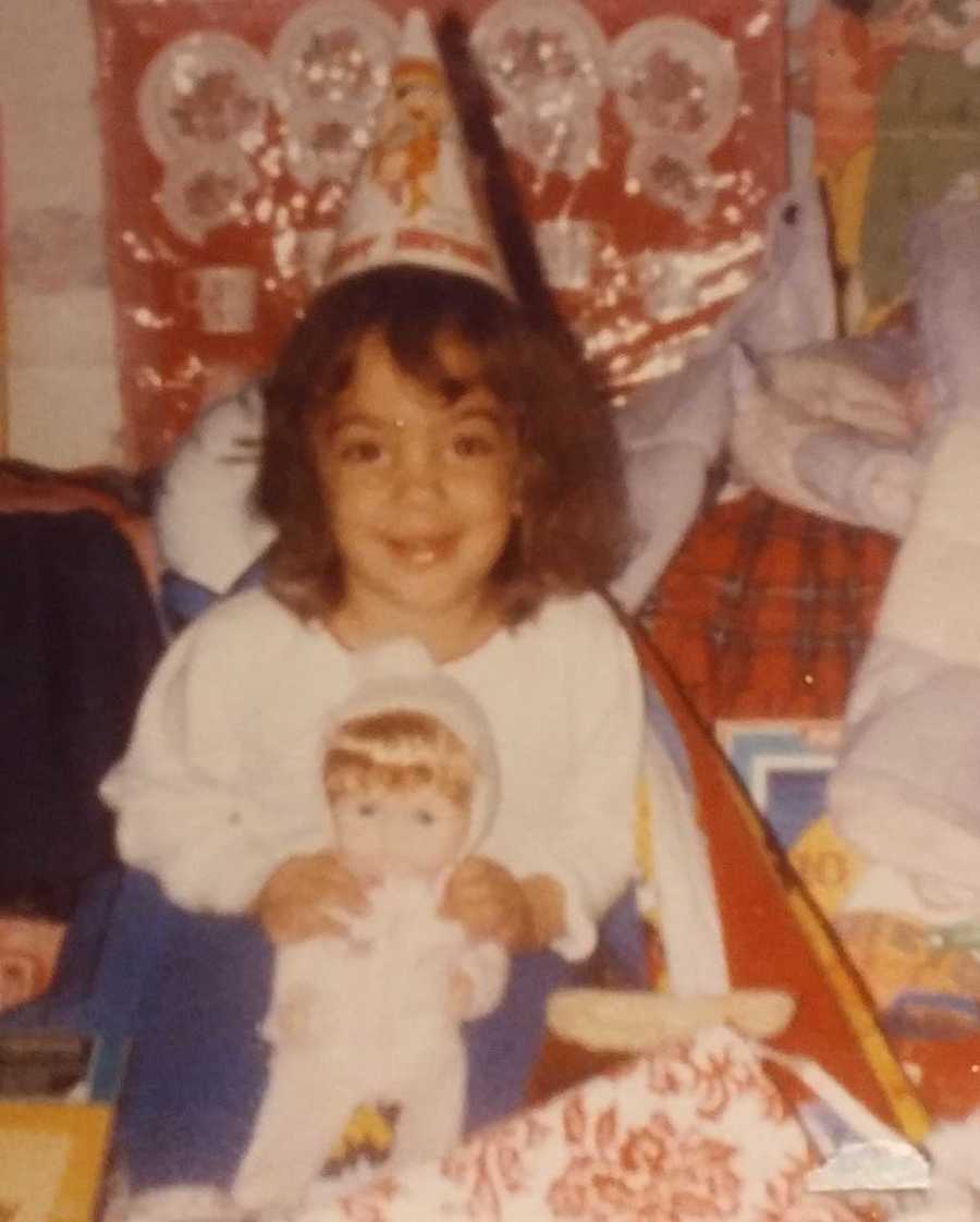 Little girl smiles as she holds baby doll with party hat on 