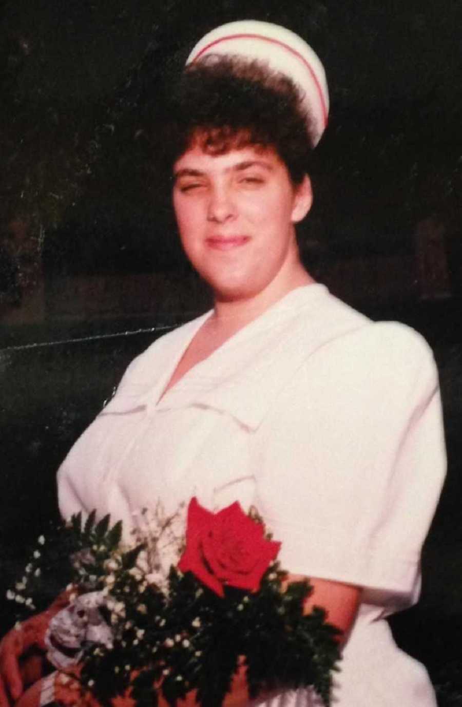 Woman smiles in nursing outfit as she holds bouquet of flowers