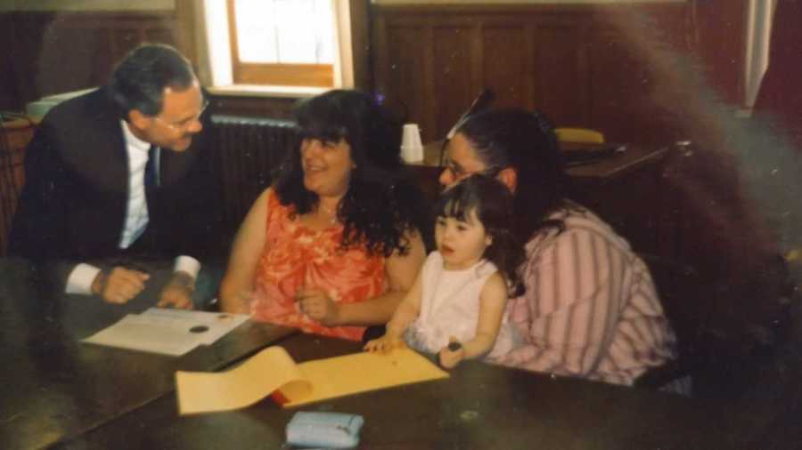 Woman sits smiling smiling at lawyer as she sits next to wife who has their daughter on her lap