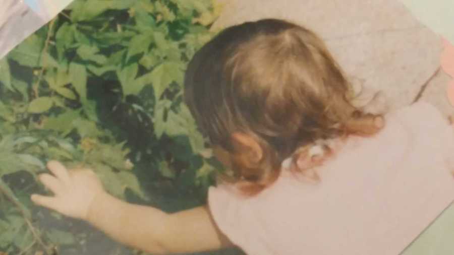 Little girl reaches her hand out to touch green plants