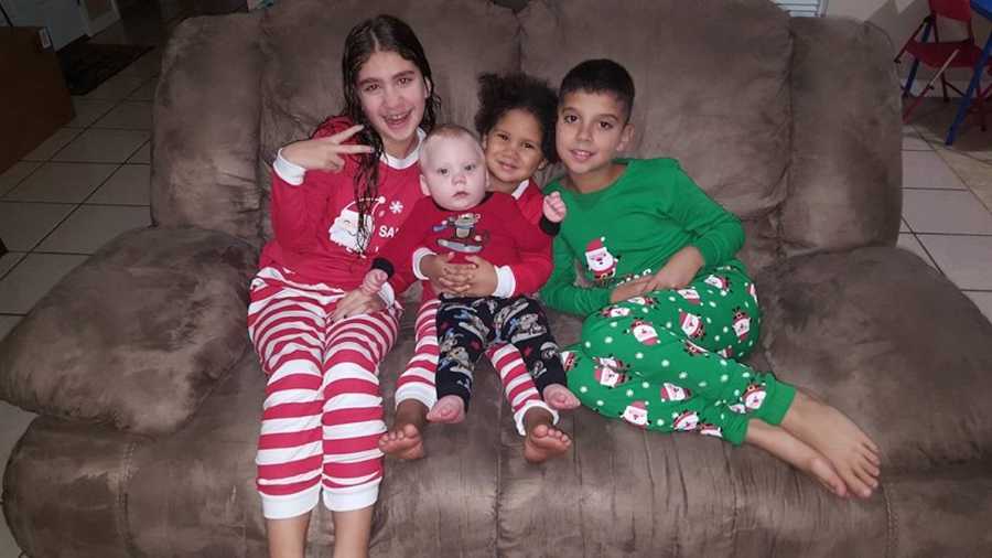 Four adopted sibling sit on couch in matching Christmas pajamas