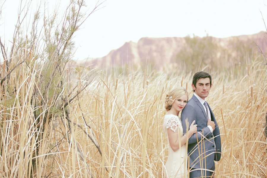 Bride and groom stand in straw field for photoshoot