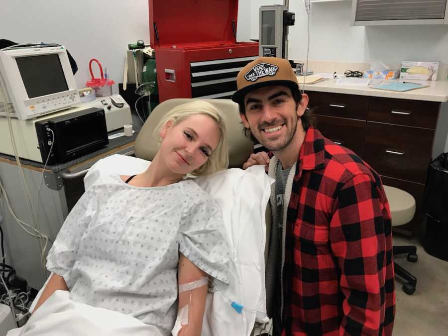 Husband kneels smiling beside wife who lays in doctor's office