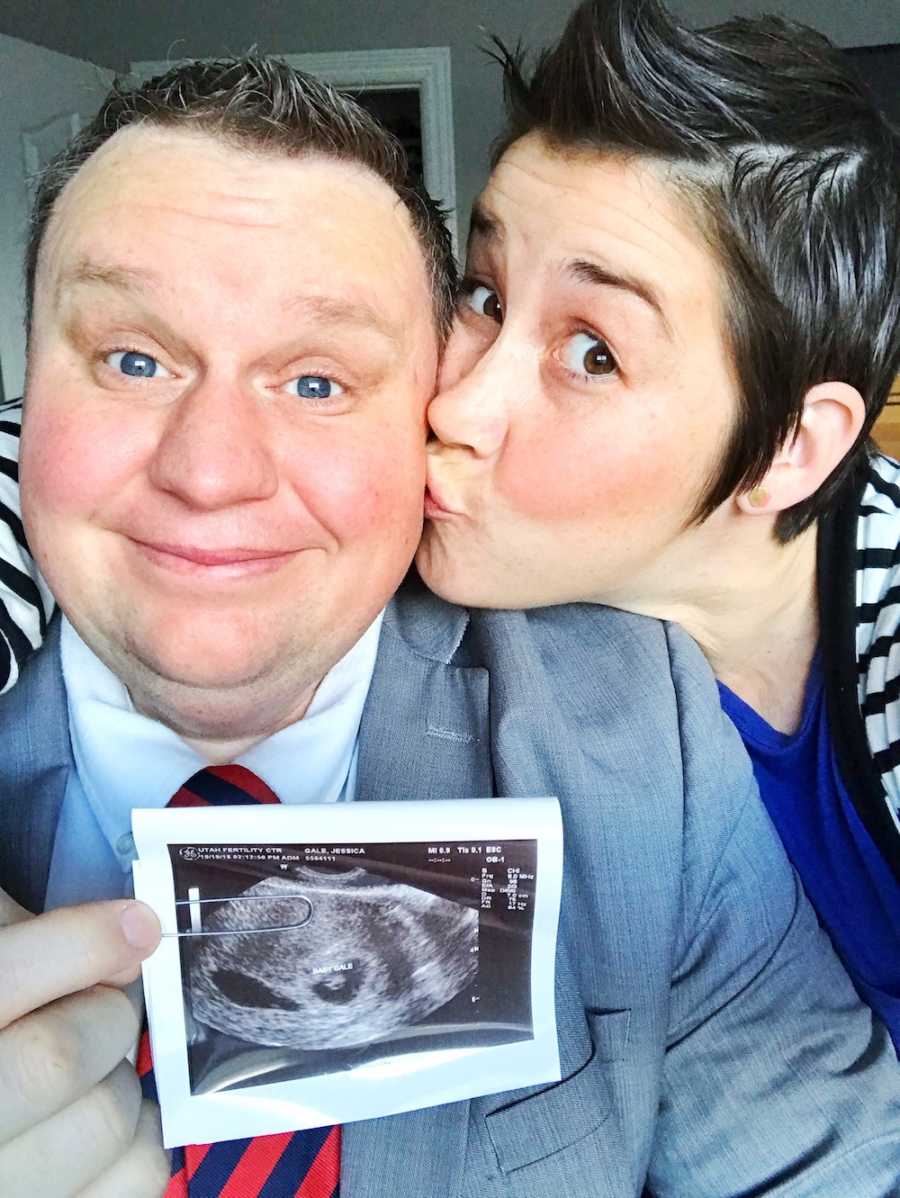Wife kisses husband on the cheek as he holds ultrasound picture