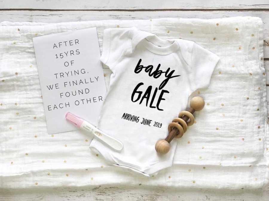 Baby onesie lays on blanket beside pregnancy test, baby rattle and sign announcing baby