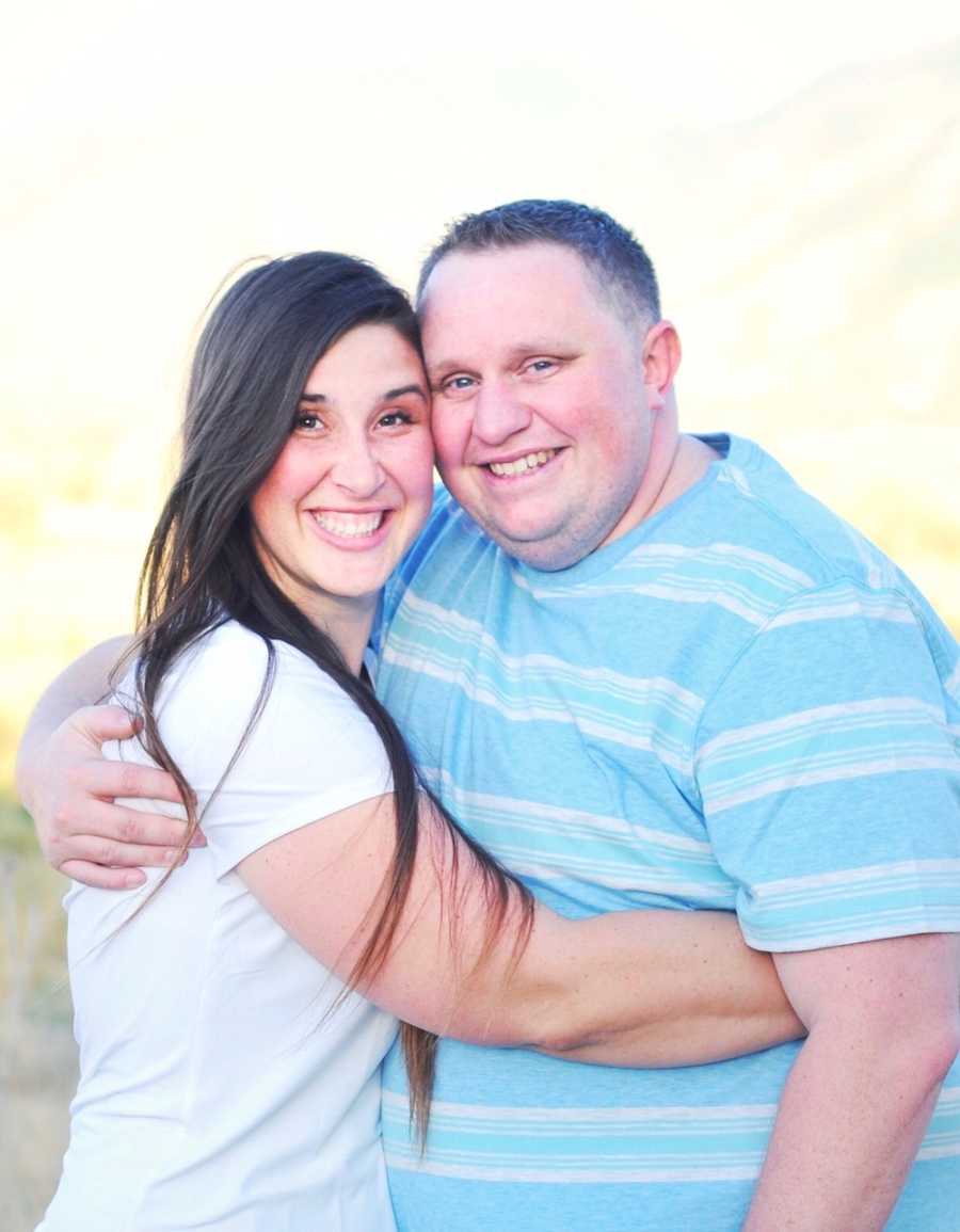 Husband and wife stands outside smiling in each others arms