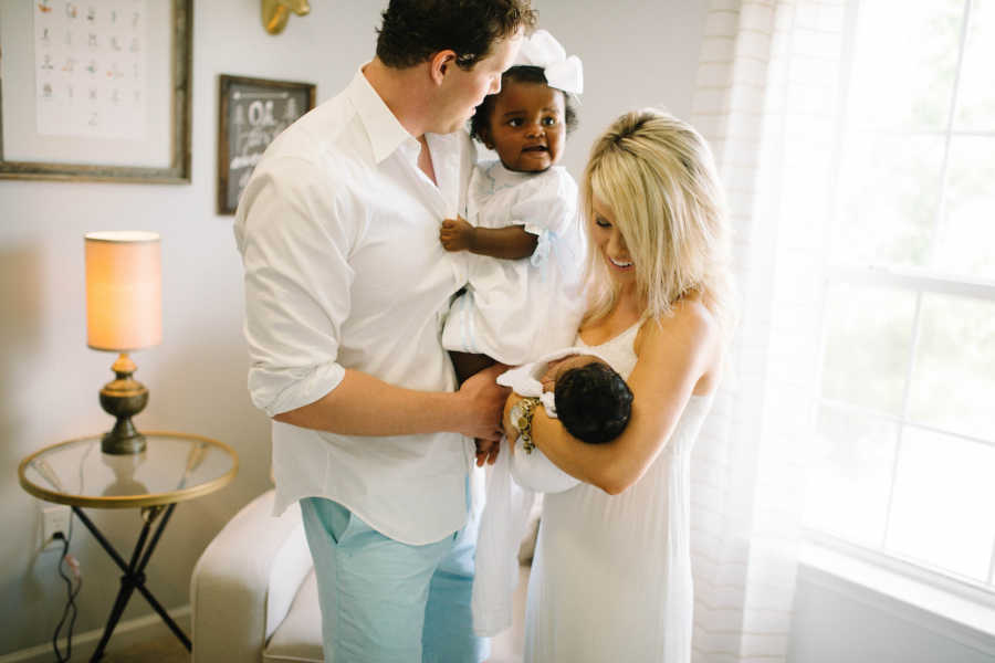 Husband and wife stand in home each holding one of their adopted children