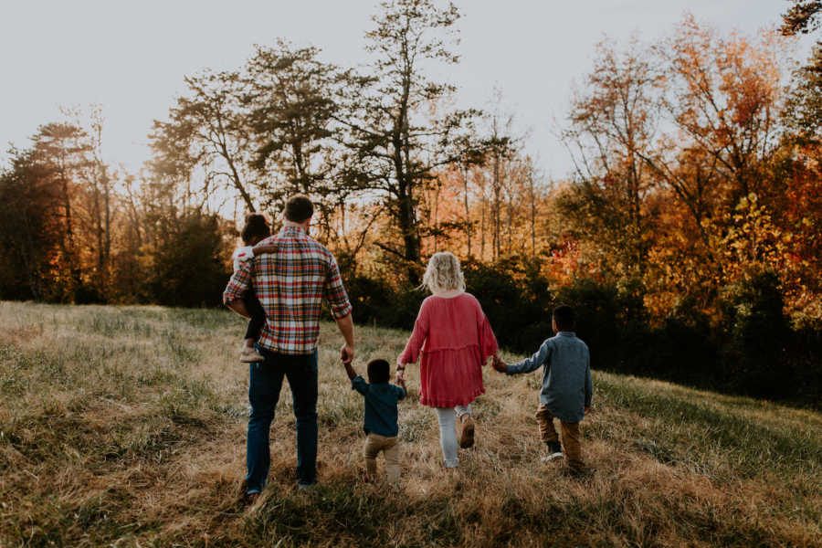 Husband and wife walk in field holding hands with their biological child and two foster children