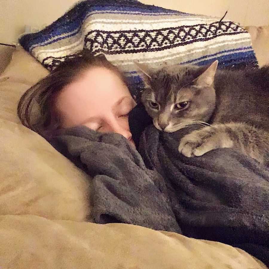 Woman lays asleep on couch while her cat lays on top of her