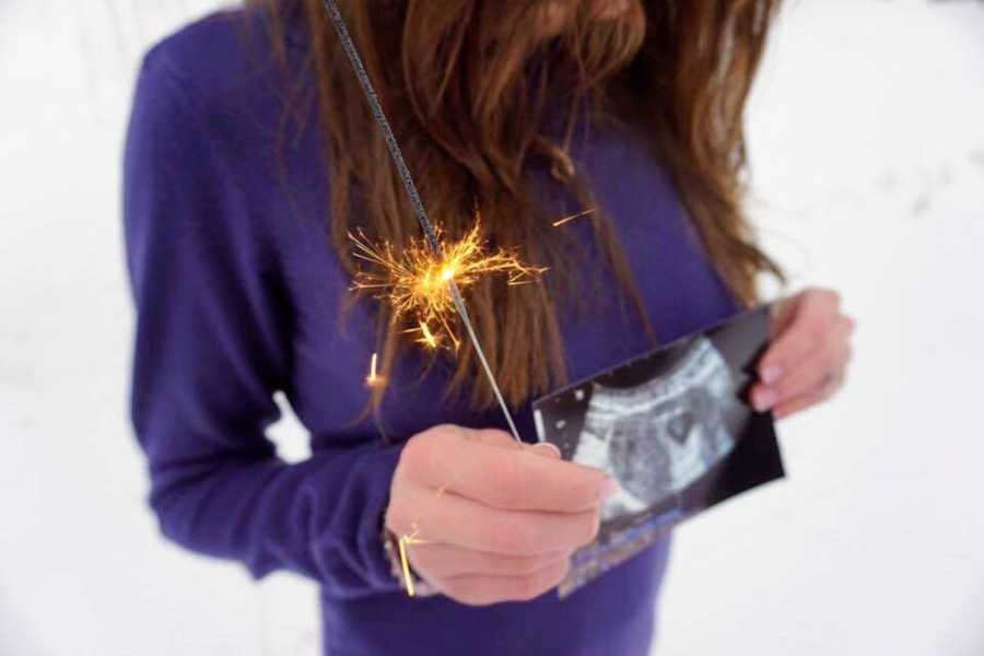 Woman holds sparkler in hand while also holding ultrasound picture in front of her