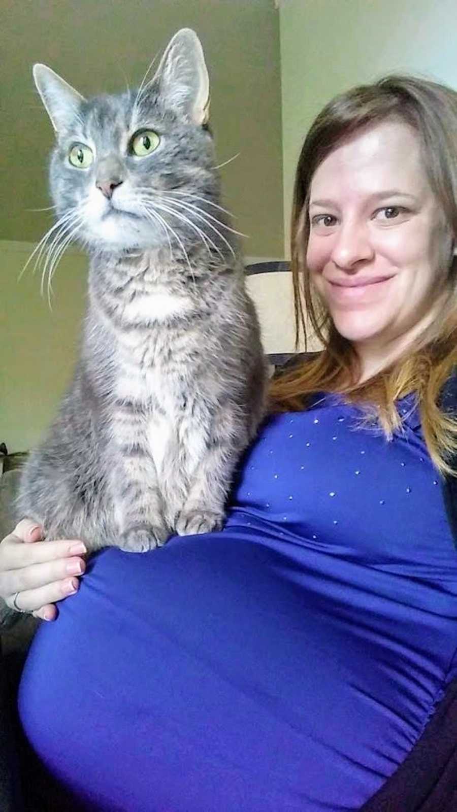 Pregnant woman smiles as her cat sits on her stomach