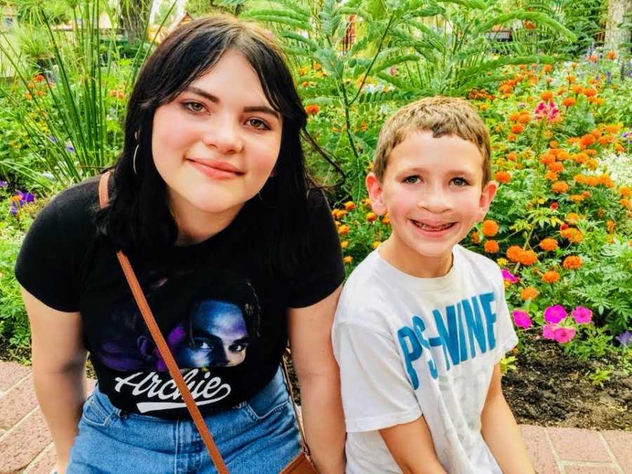 Little boy who had cleft lip and palate surgery sits smiling outside beside his older sister