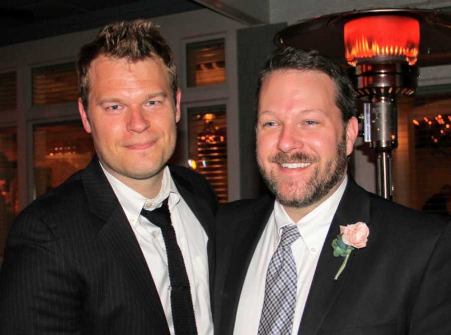 Married men stand smiling in suits 