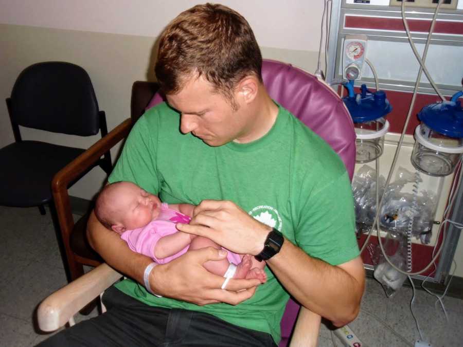 Man sits in hospital chair holding adopted newborn in his arms as she sleeps