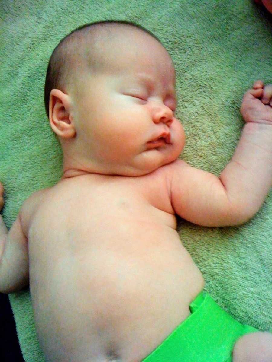 Adopted baby girl lays on her back asleep wearing green diaper
