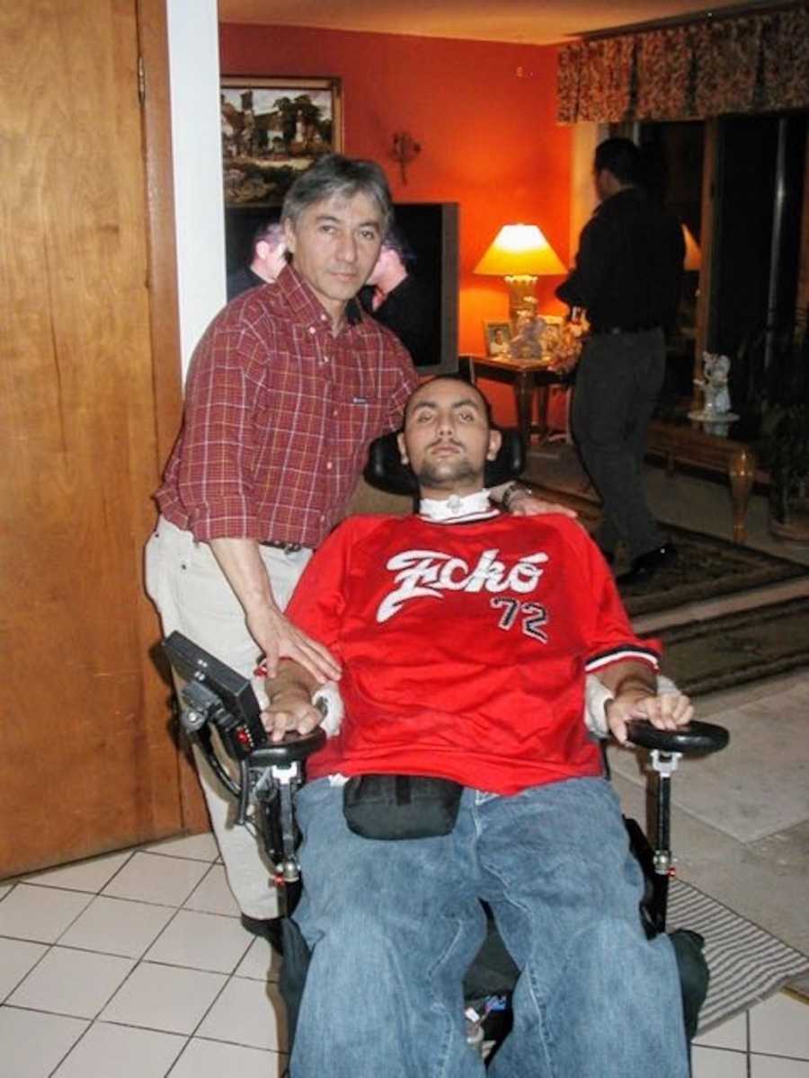 Man who was shot 5 times sits in wheel chair in home while his father stands behind him