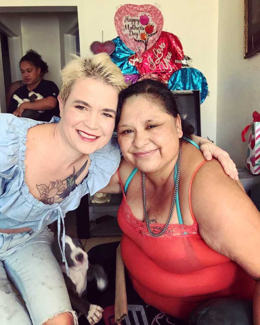 Homeless woman with bipolar disorder leans over to hug woman sitting in chair at homeless shelter