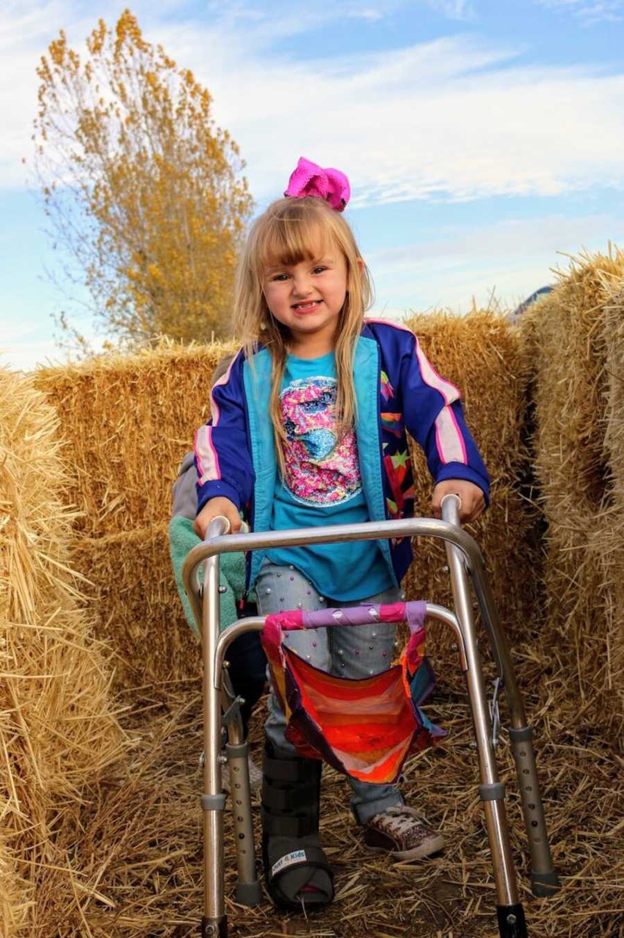 Little girl with Osteogenesis Imperfecta smiles as she walks through hay bale maze with walker