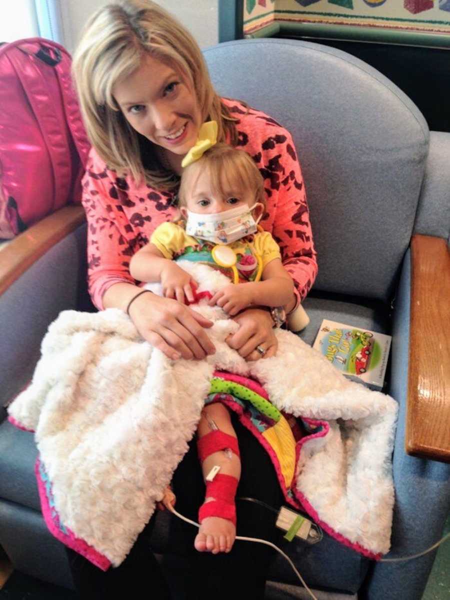 Mother sits in hospital chair with daughter in her lap who has a brace on her leg