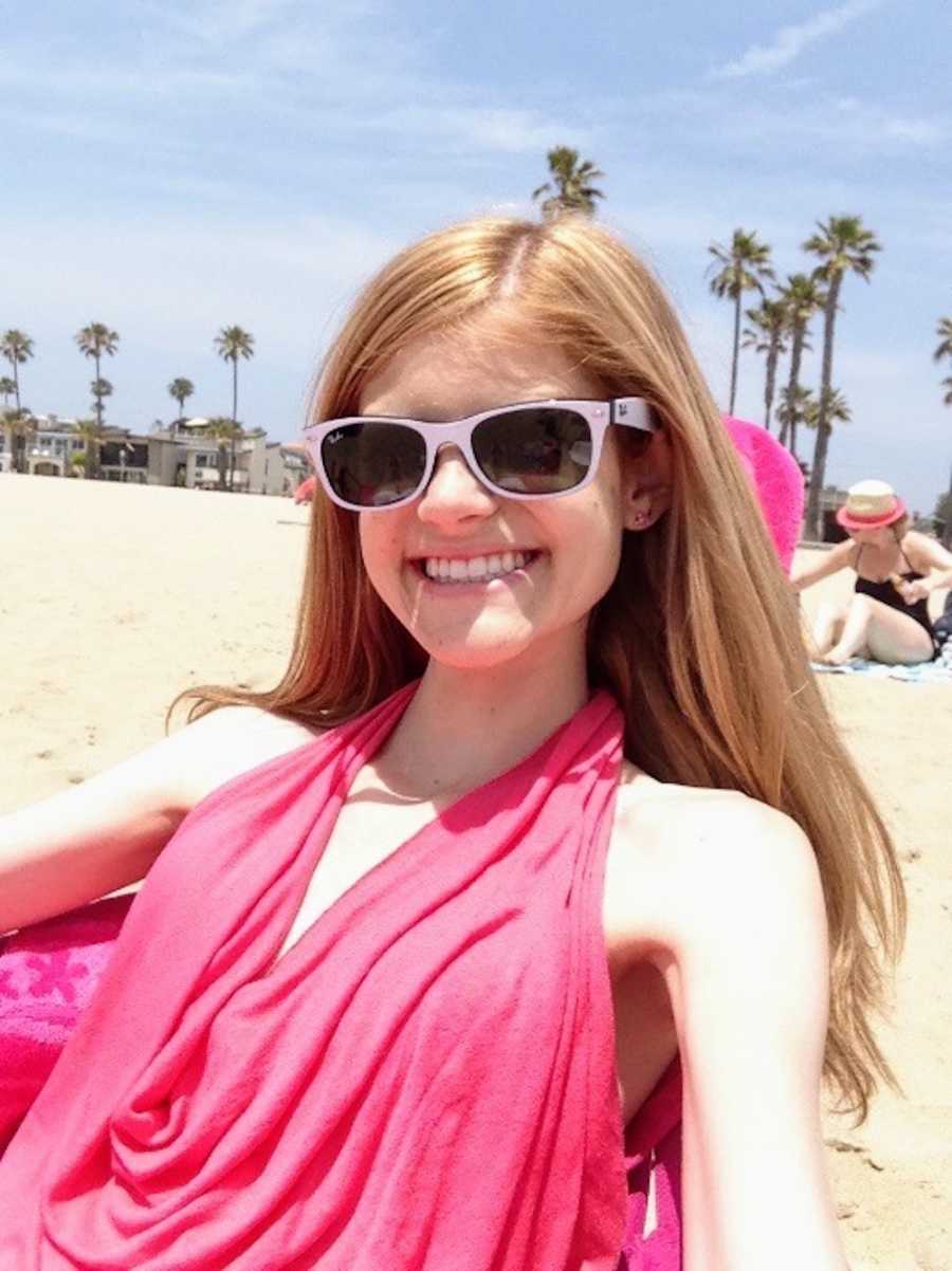 Young girl with Crohn's disease smiles as she sits in beach chair with white sunglasses on