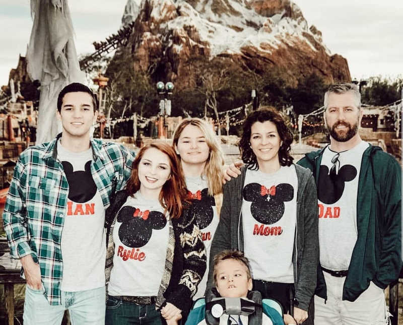 Husband and wife stand at Disney World with their four kids, one of which has cerebral palsy"