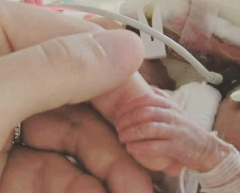 Close up of preemie baby holding finger of mother