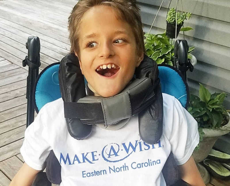 Little boy with cerebral palsy sits smiling in wheel chair wearing Make-A-Wish t-shirt