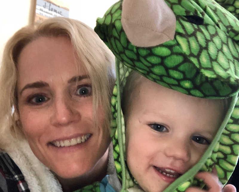 Mother smiles in selfie with son who wears dinosaur costume 