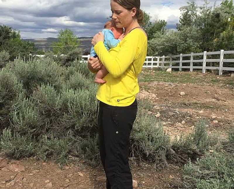 Mother stands outside in field holding baby to her chest