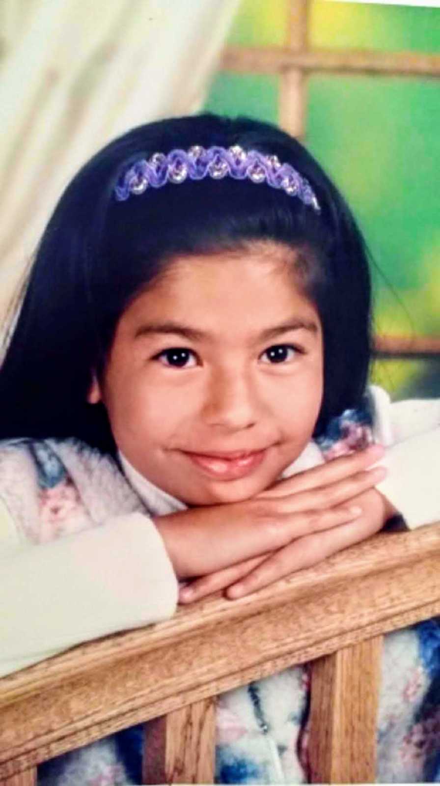 Little girl smiles as she rests chin on hands that are on railing