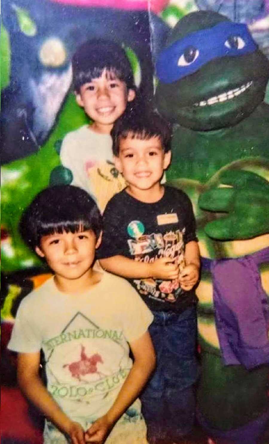 Three young brothers stand beside statue of Teenage Mutant Nina Turtle