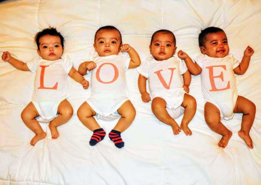 Quadruplets lay on their backs wearing onesies that spell out "Love"