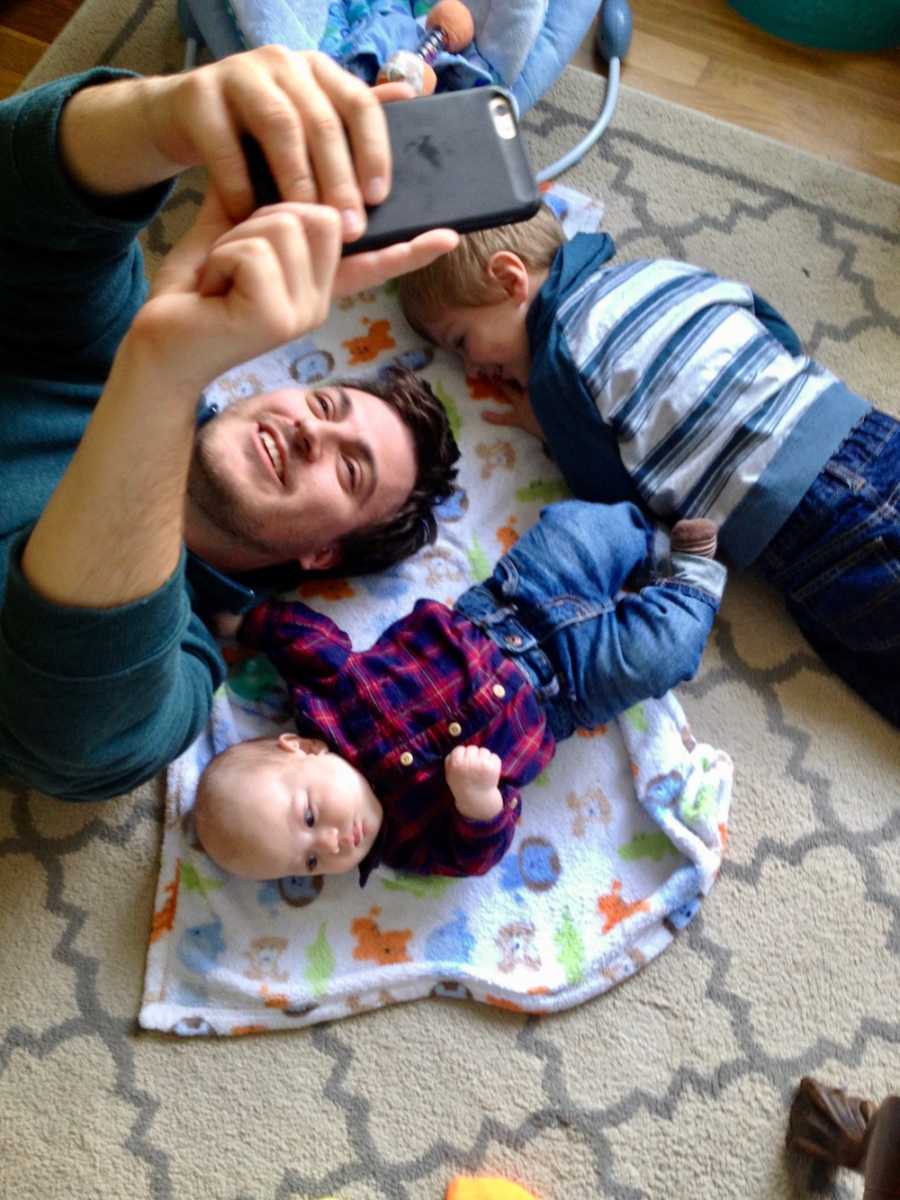 Father lays on ground taking selfie with his two young son who were diagnosed with autism