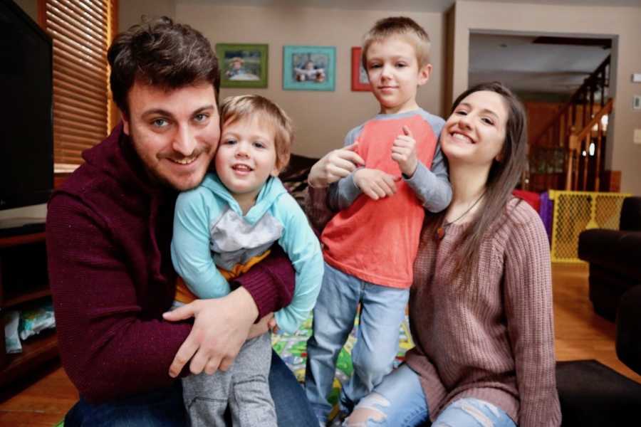 Husband and wife sit on floor of home holding their two son's with autism