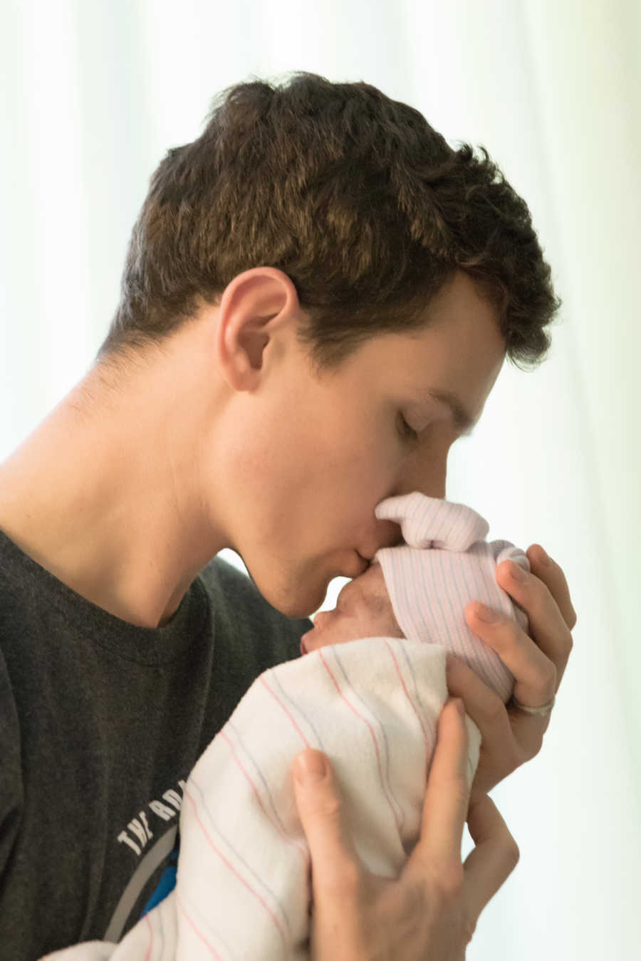 Father kisses head of newborn baby that he holds