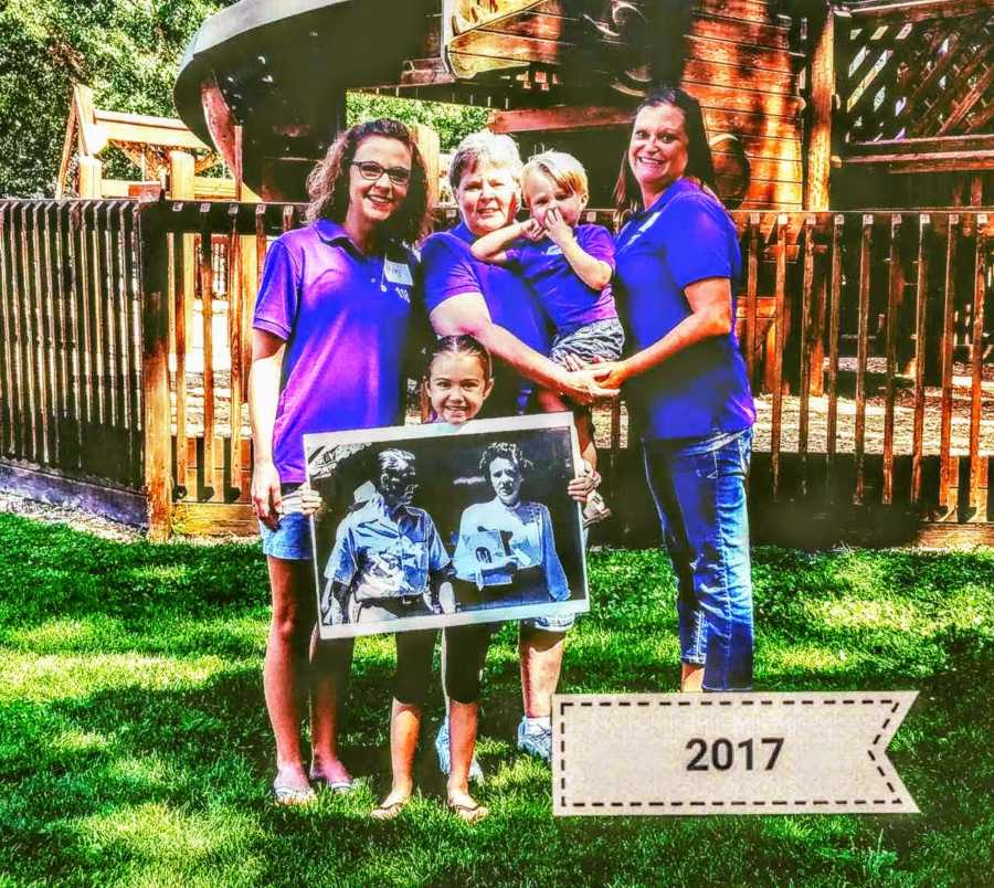 Woman stands outside beside mother sister and two little kids as one kid holds picture of her great grandparents