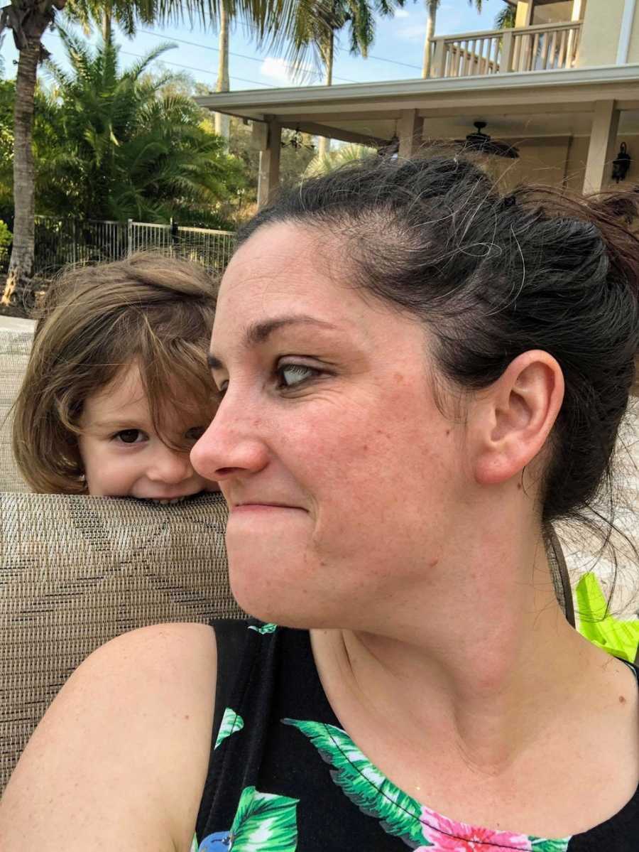 Mother takes selfie as she sits outside looking over at her feral daughter who stands behind her