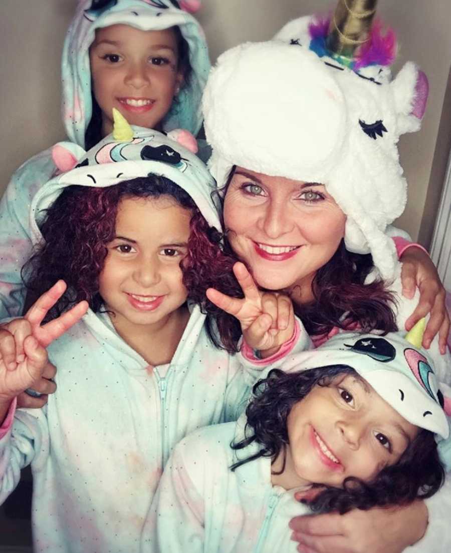 Mother smiles in selfie with three daughters who are all wearing unicorn onesies